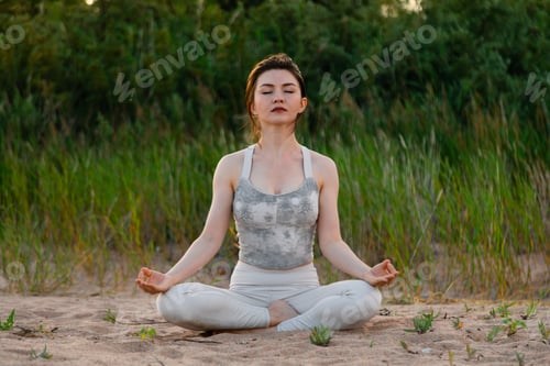 Preview: Woman practicing yoga outside in lotus pose on sand
