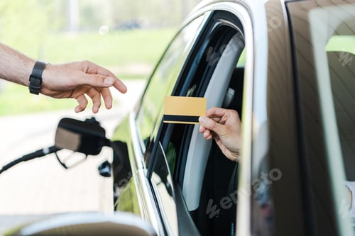 Preview: cropped view of woman in car giving credit card to worker at gas station
