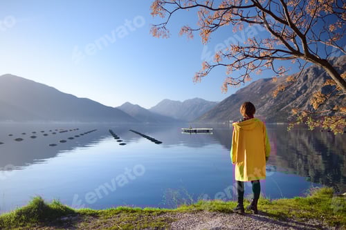 Preview: Young woman in yellow coat standing on the coast of Adriatic sea