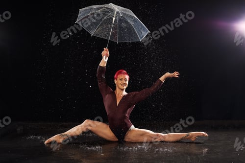 Preview: Beautiful young girl in red sportswear with umbrella in aqua studio. Drops of water spread about her
