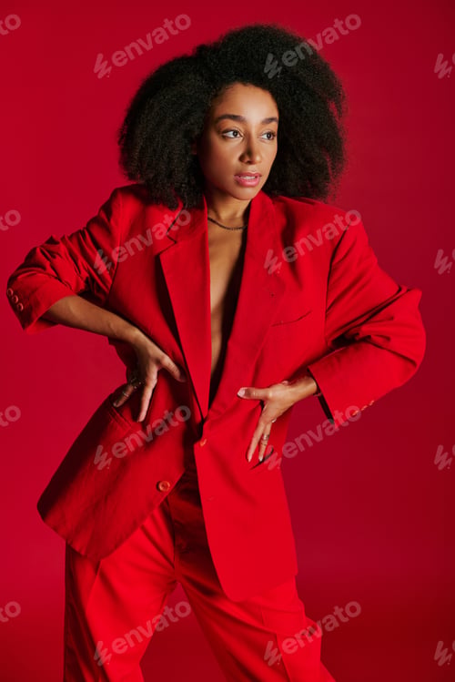 Preview: alluring african american female model in red blazer looking away on red background, fashion concept
