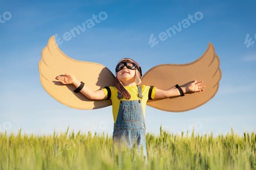 Preview: Happy child with cardboard wings playing outdoor in summer