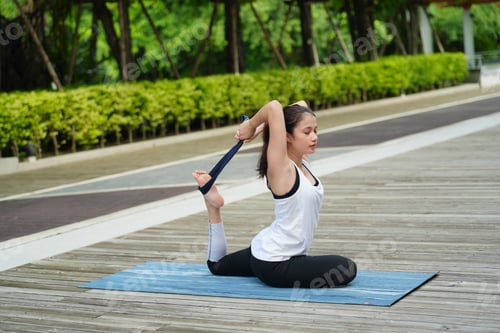 Preview: Attractive young woman in sports clothing practicing yoga balance at park.
