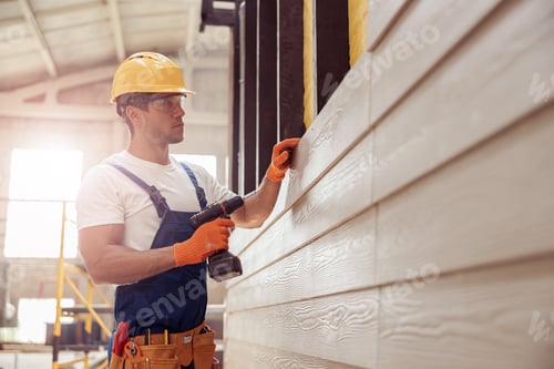 Preview: Handsome young man builder installing exterior wood siding