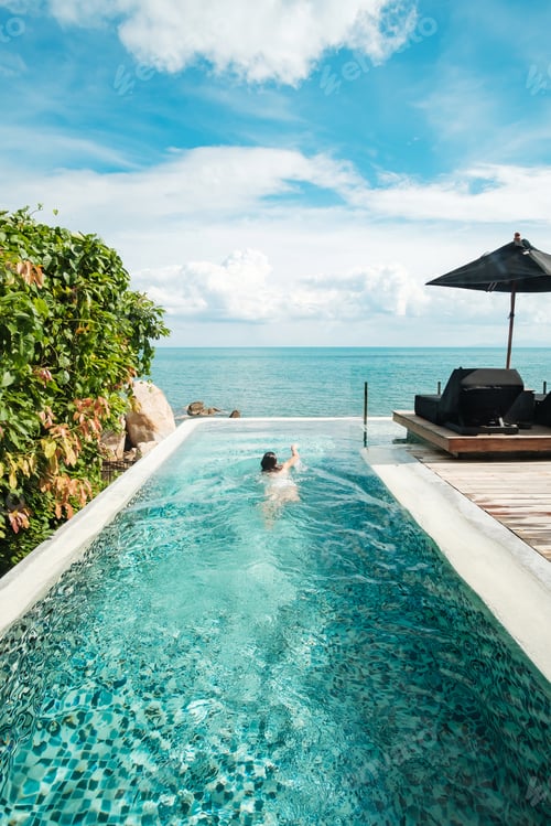 Preview: woman in luxury pool hotel against ocean front. Relaxing, summer travel, holiday, vacation concept