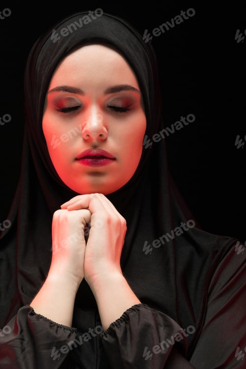 Preview: Portrait of beautiful serious young muslim woman wearing black hijab with closed eyes as praying