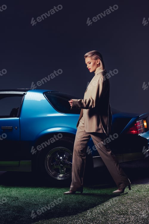Preview: attractive and stylish woman in suit walking near retro car