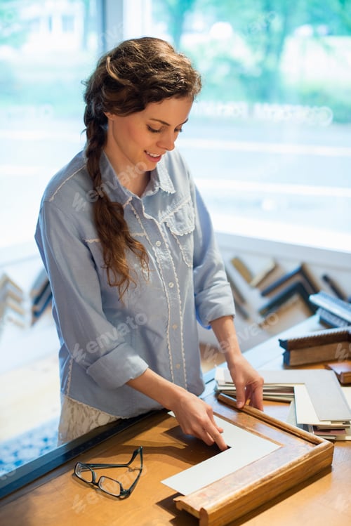 Preview: A woman in a picture framer's workshop, choosing frames and cardboard mounts. Surrounded by samples.