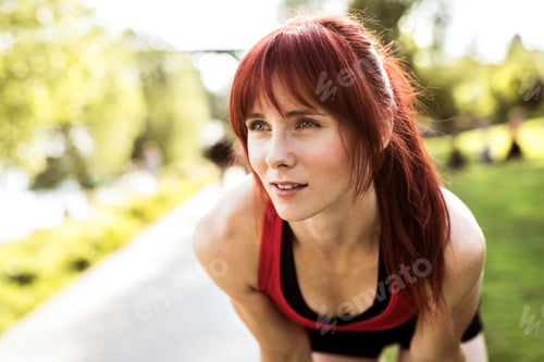 Preview: Beautiful young runner on a path in the city park, resting.