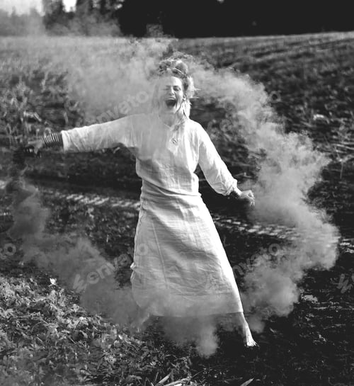Preview: Happy woman in white dress with green smoke bomb dancing on muddy field