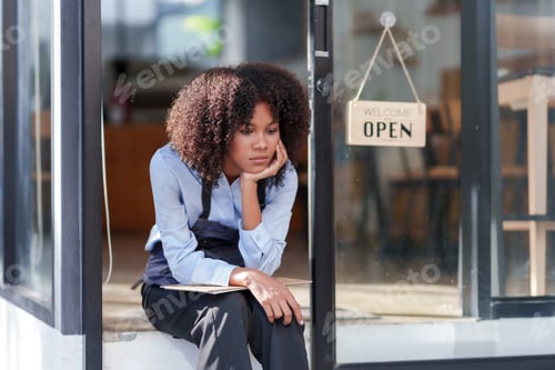 Preview: Female shopkeeper sitting stressed out at the store entrance frustrated by the economic impact.