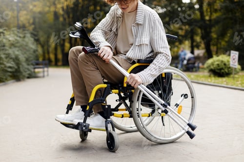 Preview: Smiling young man in a wheelchair holds a crutch in his hands.