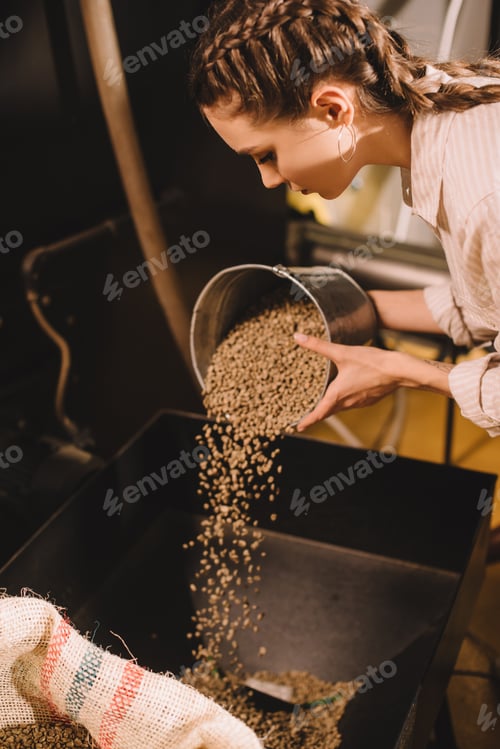 Preview: side view of young worker pouring coffee beans into container