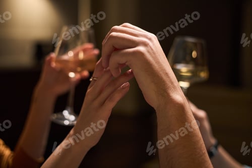 Preview: Young Adult Couple Holding Hands While Toasting with Wine Glasses