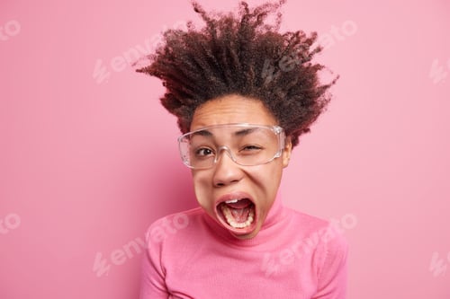 Preview: Studio shot of emotive mad curly haired Afro American woman winks eye keeps mouth wide opened exclai