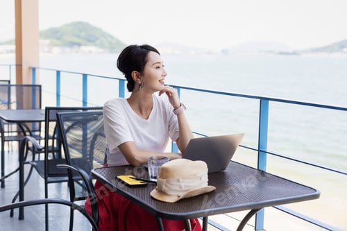 Preview: Female Japanese professional sitting on balcony of a co-working space, using laptop computer.