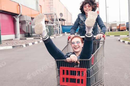 Preview: ✓ ↟ Funny happy teenage girls in denim clothes have fun and ride on the shopping cart