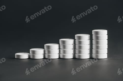 Preview: close up view of arranged stacks of white pills placed in rows on grey