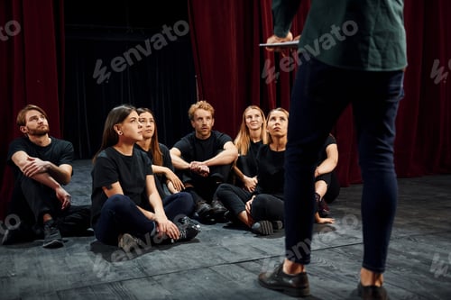 Preview: Sitting and listening to man. Group of actors in dark colored clothes on rehearsal in the theater
