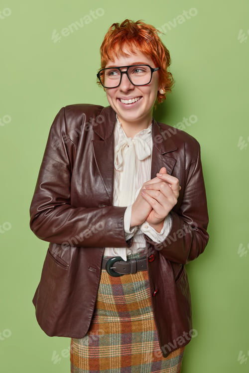 Preview: Lovely positive redhead young woman wears spectacles white blouse leather jacket and checkered skirt