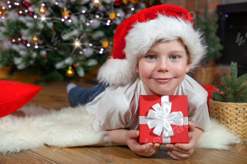 Vorschau: Frohe Weihnachten, Kinder. Ein Junge in einer Weihnachtsmütze mit einem Geschenk vom Weihnachtsmann, in der Nähe eines Weihnachtsbaums mit