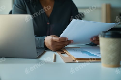 Preview: Multiracial woman sitting at table and holding papers in her hands