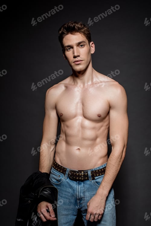 Preview: sexy young man with muscular torso in jeans holding biker jacket on black background
