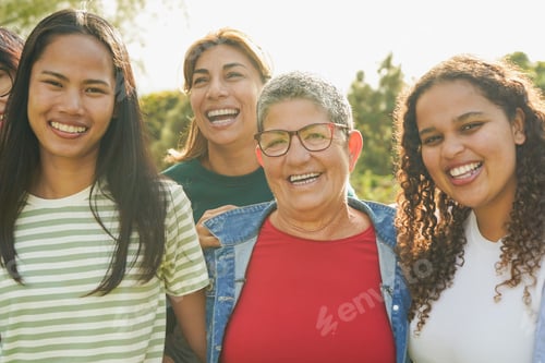 Preview: Group of multi generational women hugging each other while smiling on camera at city park