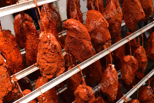 Preview: pieces of pork delicacies in paprika and spices are hung on a metal rack in a meat-packing plant or