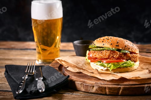 Preview: Delicious hot spicy black burger with chili pepper and glass of beer on cutting board on white wood