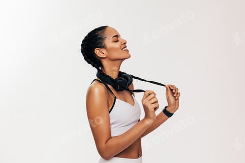 Preview: Side view of fitness woman standing on white background with closed eyes holding her dutch braids
