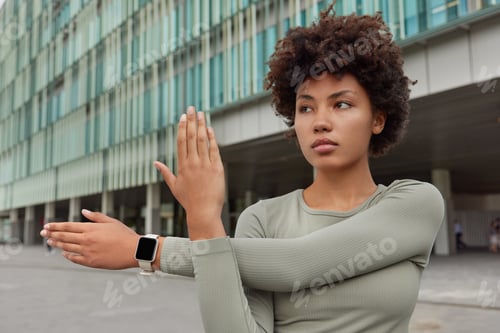 Vista previa: Determined beautiful curly haired sportswoman does warm up exercises stretches arms before workout w