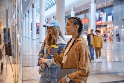Preview: Teenage girls friends looking through showcase window in shopping mall