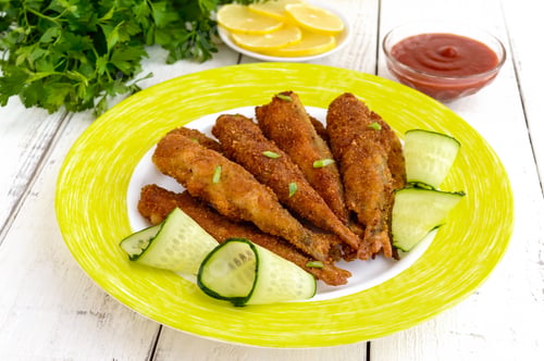 Preview: Deep frying small fish capelin on a plate on white wooden background.