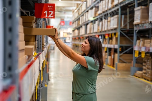 Preview: Woman customer looking up and pulling product on shelf while shopping in storage of shop