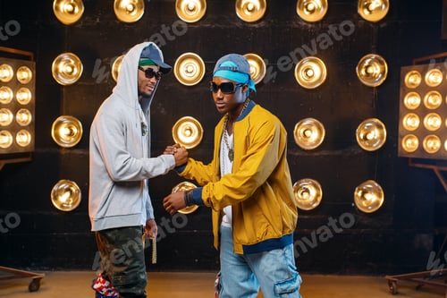 Preview: Two black rappers in caps hugging on stage