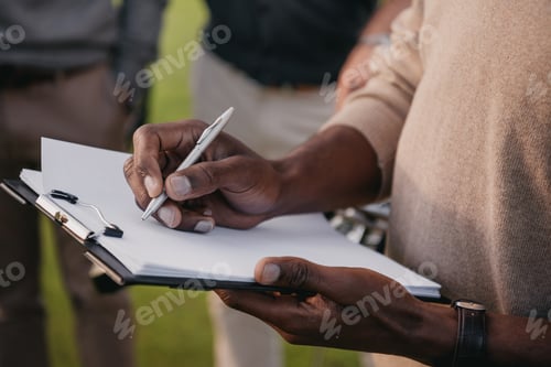 Preview: cropped view of african american man writing something on paper in clipboard