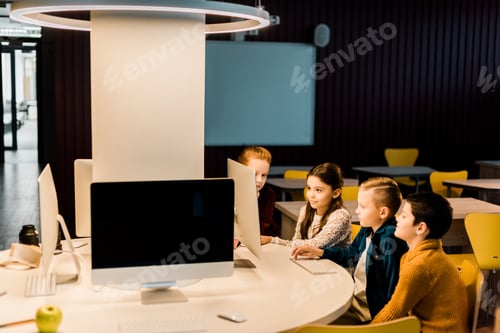 Preview: adorable schoolchildren sitting and using desktop computer together in modern library
