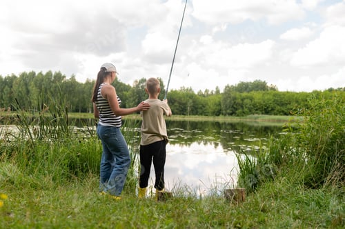 Preview: Mother and teenage son fishing together on lake shore, enjoying summer day in nature