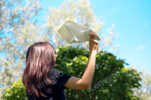 Preview: Young woman throwing a paper plane in the air on a sunny day