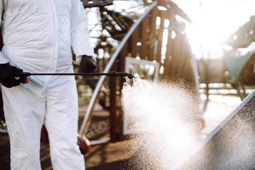 Preview: Man wearing protective suit disinfecting the playground in the sun with spray. Covid -19. Cleaning.
