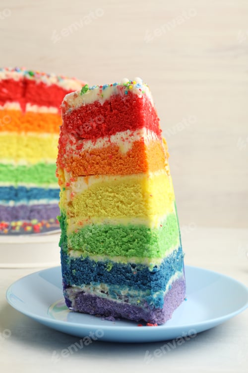 Preview: Piece of delicious rainbow cake on white table, closeup