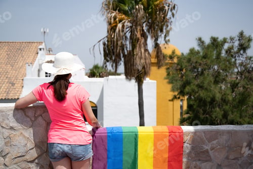 Preview: Woman from behind with hat looking from terrace next to lgtbi flag