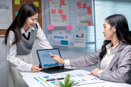 Preview: Two businesswomen working with charts and graphs on tablet and papers in modern office