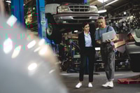 Preview: Senior male mechanic in uniform checking and diagnostic car while talking to young woman