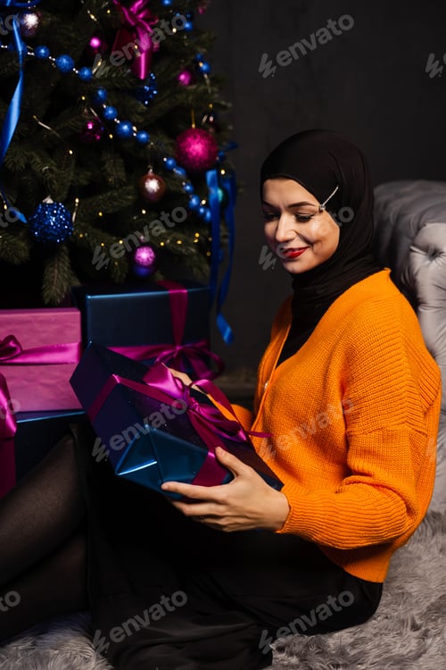Preview: Muslim woman by New Year tree holding festive present