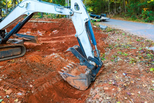 Preview: Excavator digging trench in wooded area along gravel road during works daytime operations