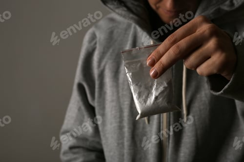 Preview: Drug dealer holding bag with cocaine on dark background, closeup. Space for text