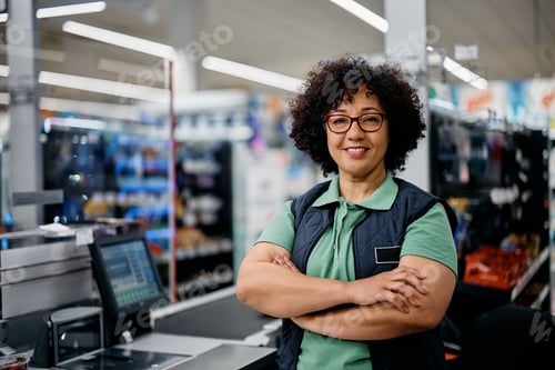 Preview: Happy supermarket cashier with her arms crossed looking at camera.