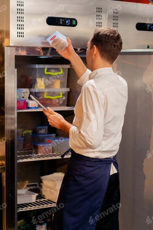Preview: professional kitchen chef looks into the fridge and chooses ingredients for cooking food concept